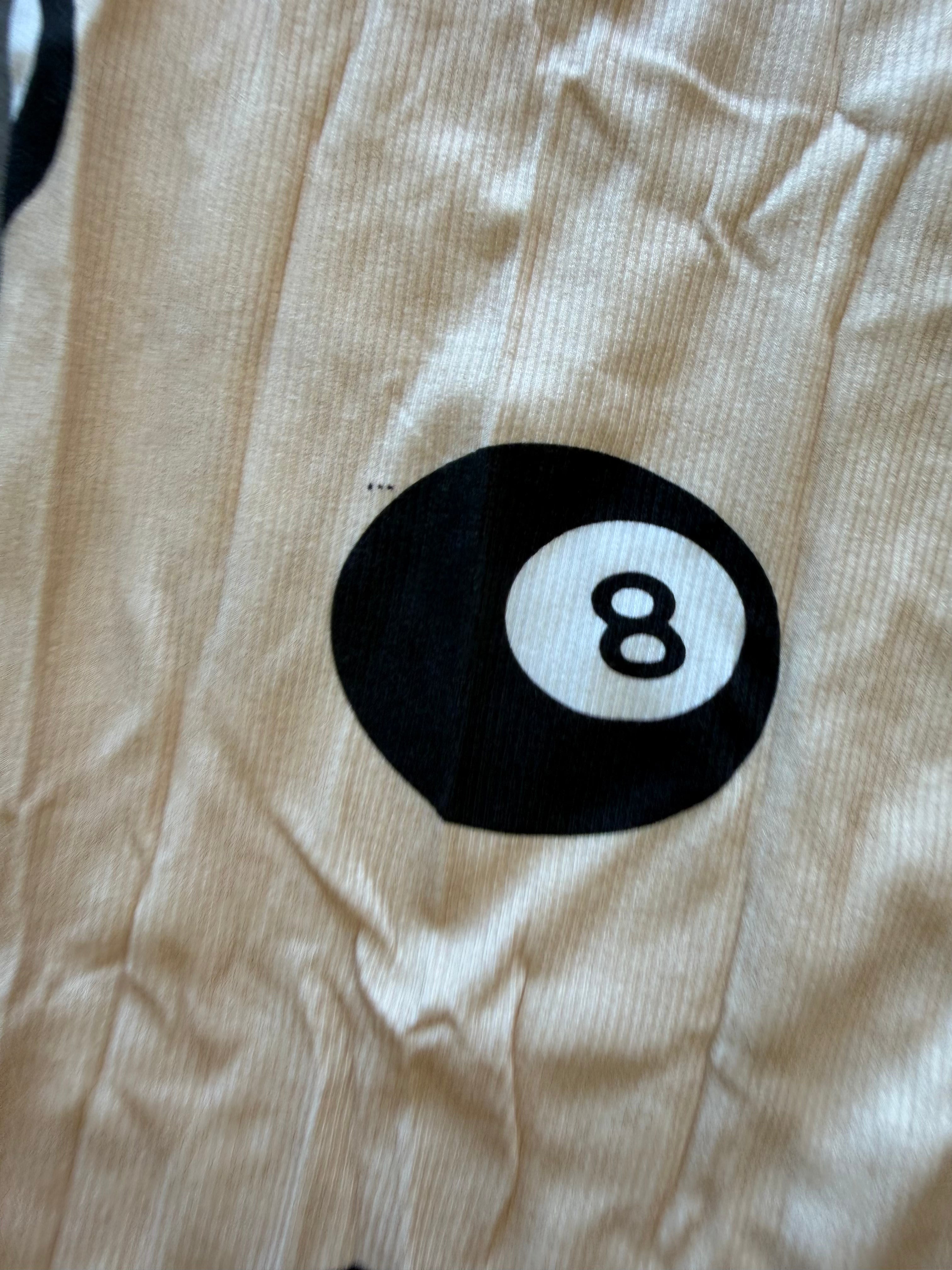 Close-up of a beige ribbed fabric garment featuring a black and white 8-ball pool icon printed on the front