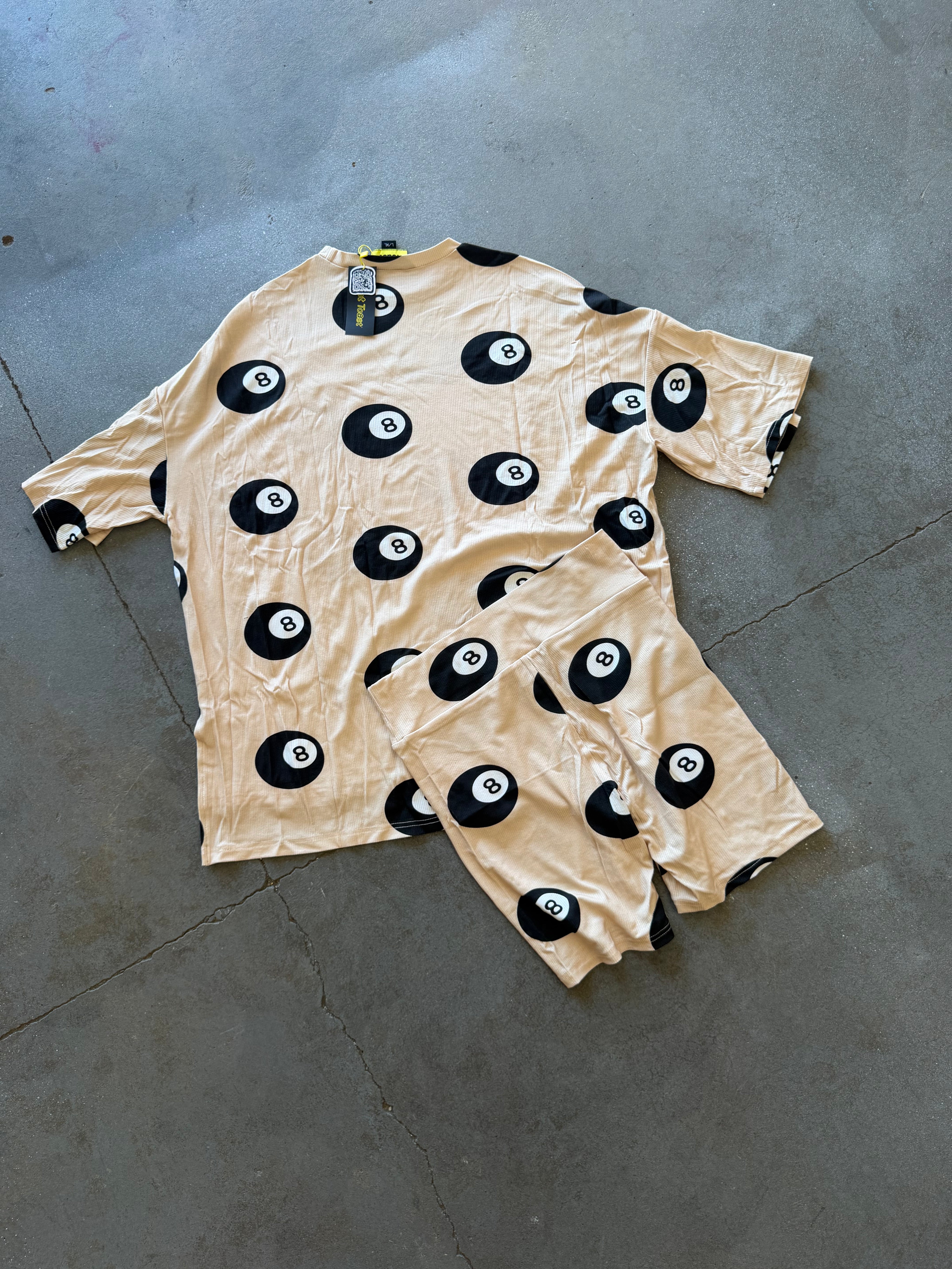 A matching beige short-sleeve top and shorts set with a black and white 8-ball pattern, laid flat on a gray concrete floor