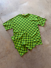A two-piece matching set consisting of a short-sleeve t-shirt and shorts, both featuring a green and dark green checkerboard pattern, laid flat on a concrete floor