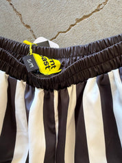 Close-up of a black and white vertically striped garment, likely shorts or a skirt, showing a dark brown elastic waistband with a yellow tag.