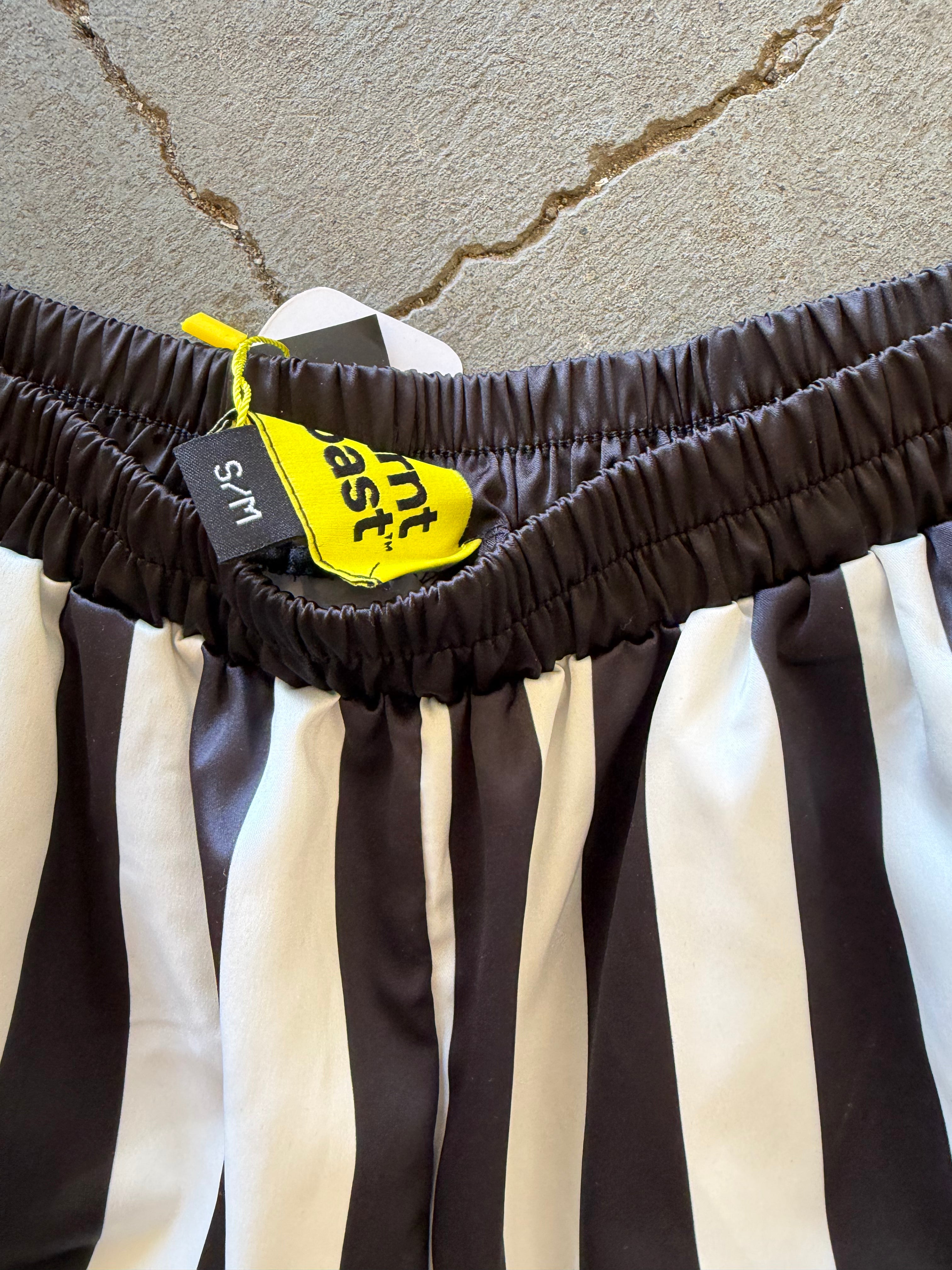 Close-up of a black and white vertically striped garment, likely shorts or a skirt, showing a dark brown elastic waistband with a yellow tag.