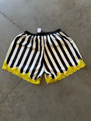 Black and white striped shorts with bright yellow lace trim at the hem, laid flat on a gray concrete floor