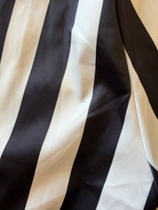 A close-up of a black and off-white vertically striped fabric with a satin-like sheen and soft folds