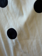 A close-up of a ribbed fabric with a black polka dot pattern on an off-white background