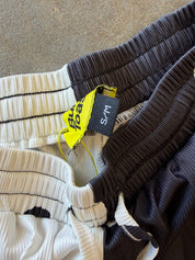 Close-up of pleated athletic shorts in multiple colors, including black, white, and dark gray, with a yellow and black size tag reading S/M