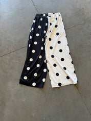 A pair of wide-leg cropped pants laid flat on a gray concrete floor, featuring a split design with black and white polka dots on each leg