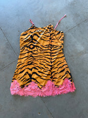 A sleeveless camisole-style top with a tiger-stripe print in orange and black, featuring thin pink straps and a bright pink fringed hem, laid flat on a gray concrete floor