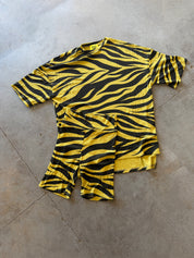 A yellow and black tiger-striped short-sleeve t-shirt and matching shorts set laid flat on a gray concrete floor