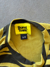 Close-up of a green and black striped ribbed knit sweater with a visible Burnt Toast brand label and size S/M tag, laid flat on a gray textured surface
