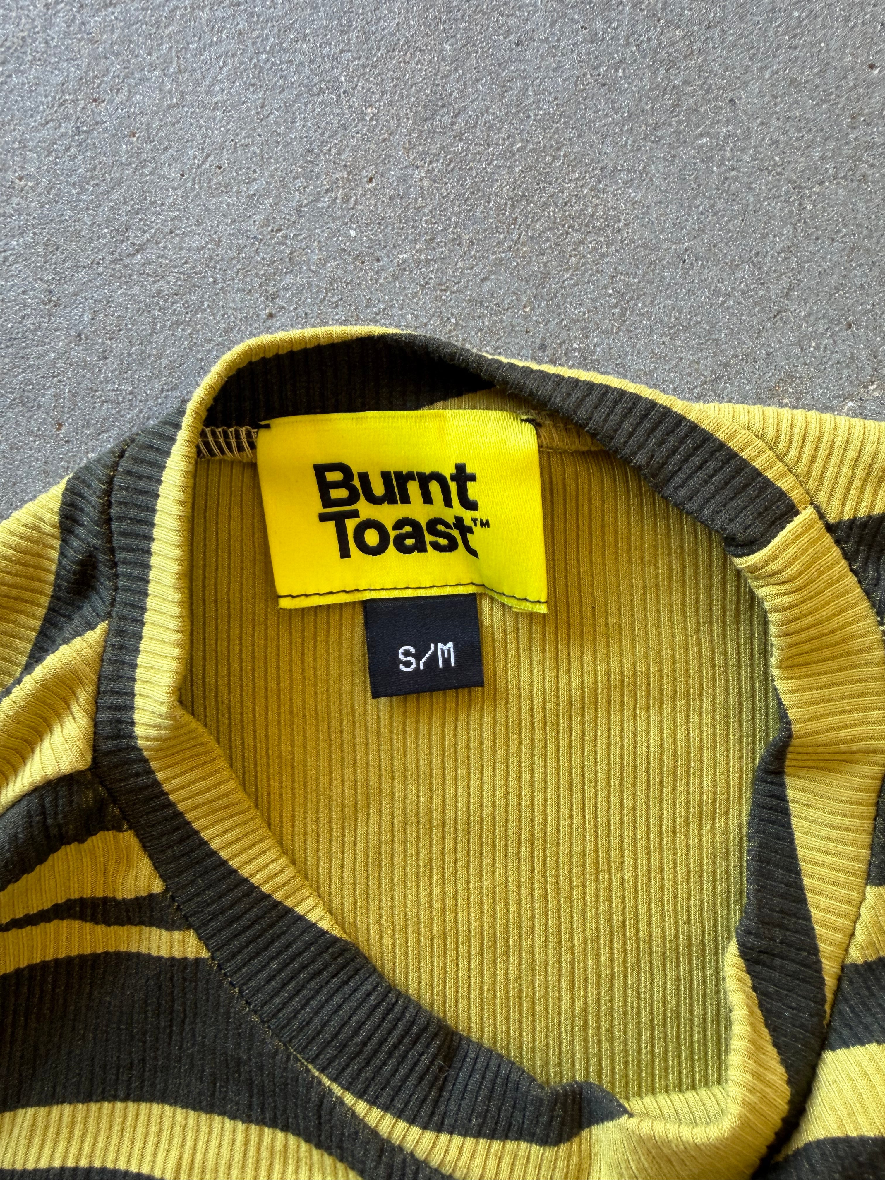 Close-up of a green and black striped ribbed knit sweater with a visible Burnt Toast brand label and size S/M tag, laid flat on a gray textured surface