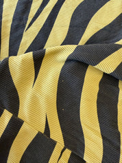 A close-up of a ribbed fabric with a bold black and mustard yellow abstract wavy pattern