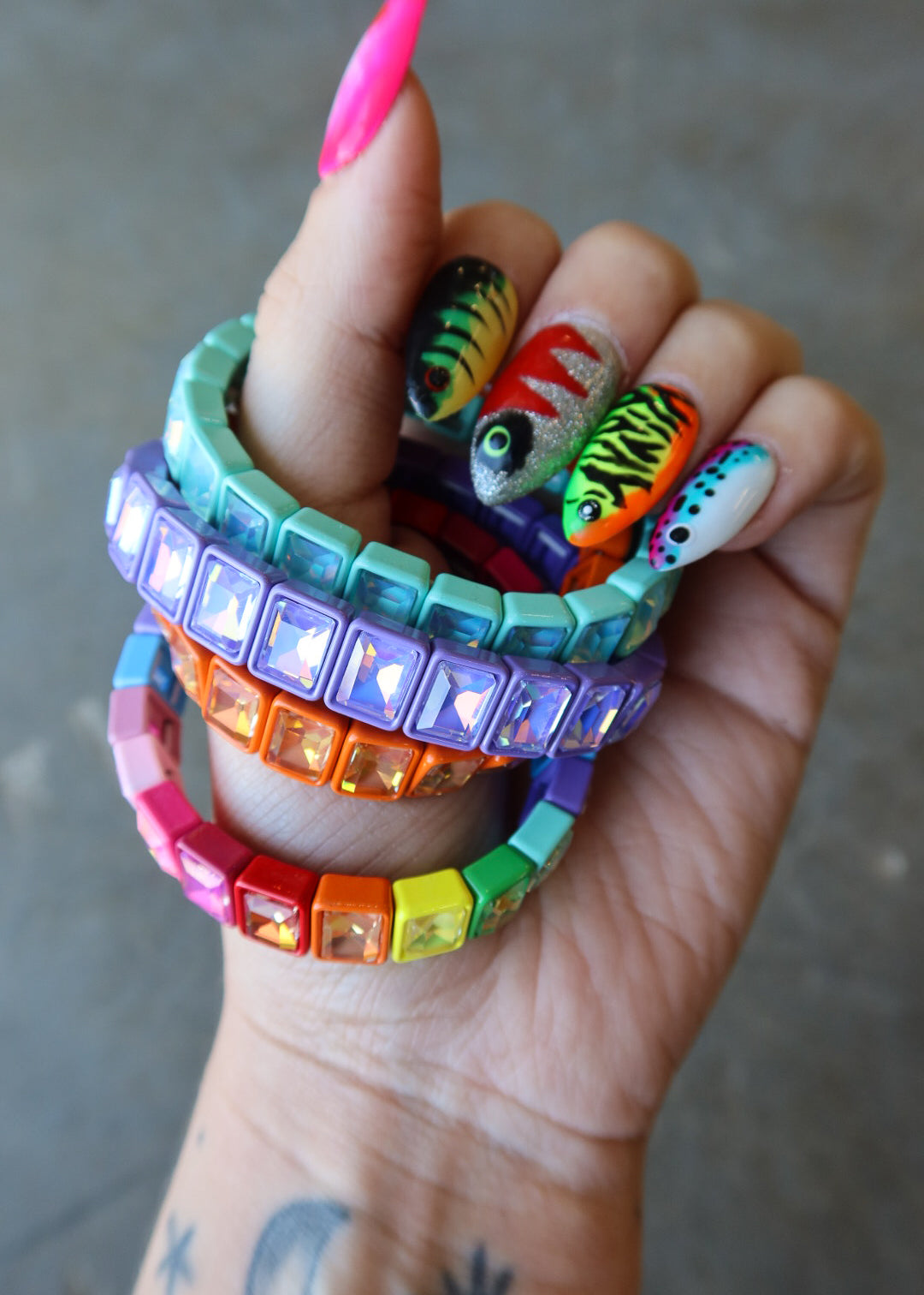 A close-up of a hand holding a stack of chunky, colorful beaded bracelets with rhinestones. The bracelets feature vibrant rainbow colors including pink, orange, yellow, green, blue, and purple, with some featuring fish designs on the front
