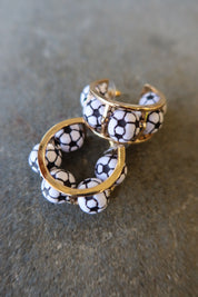 A pair of gold hoop earrings decorated with small white and black soccer ball beads, resting on a textured gray surface