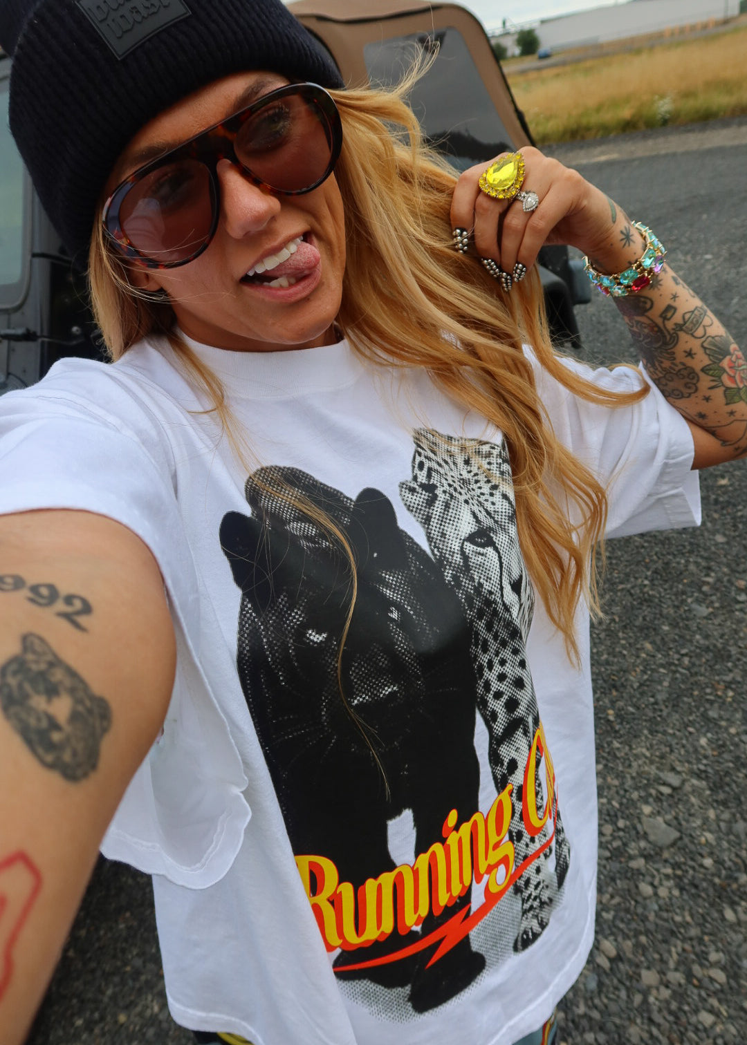 A woman taking a selfie outdoors wearing a white graphic t-shirt with a black leopard and leopard print and the words 'Running C