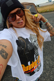 A woman taking a selfie outdoors wearing a white graphic t-shirt with a black leopard and leopard print and the words 'Running C