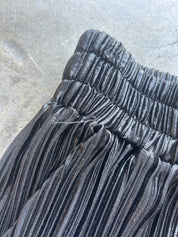 Close-up of a black pleated skirt with a gathered elastic waistband, laid flat on a gray concrete surface