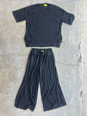 A black short-sleeve t-shirt and matching black wide-leg pants laid flat on a gray concrete floor