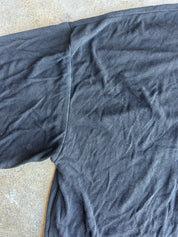 A close-up of a dark charcoal gray ribbed knit fabric, likely a t-shirt body, laid flat on a textured concrete surface