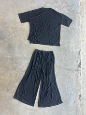 A black short-sleeve cropped T-shirt and matching black wide-leg pants laid flat on a textured concrete floor