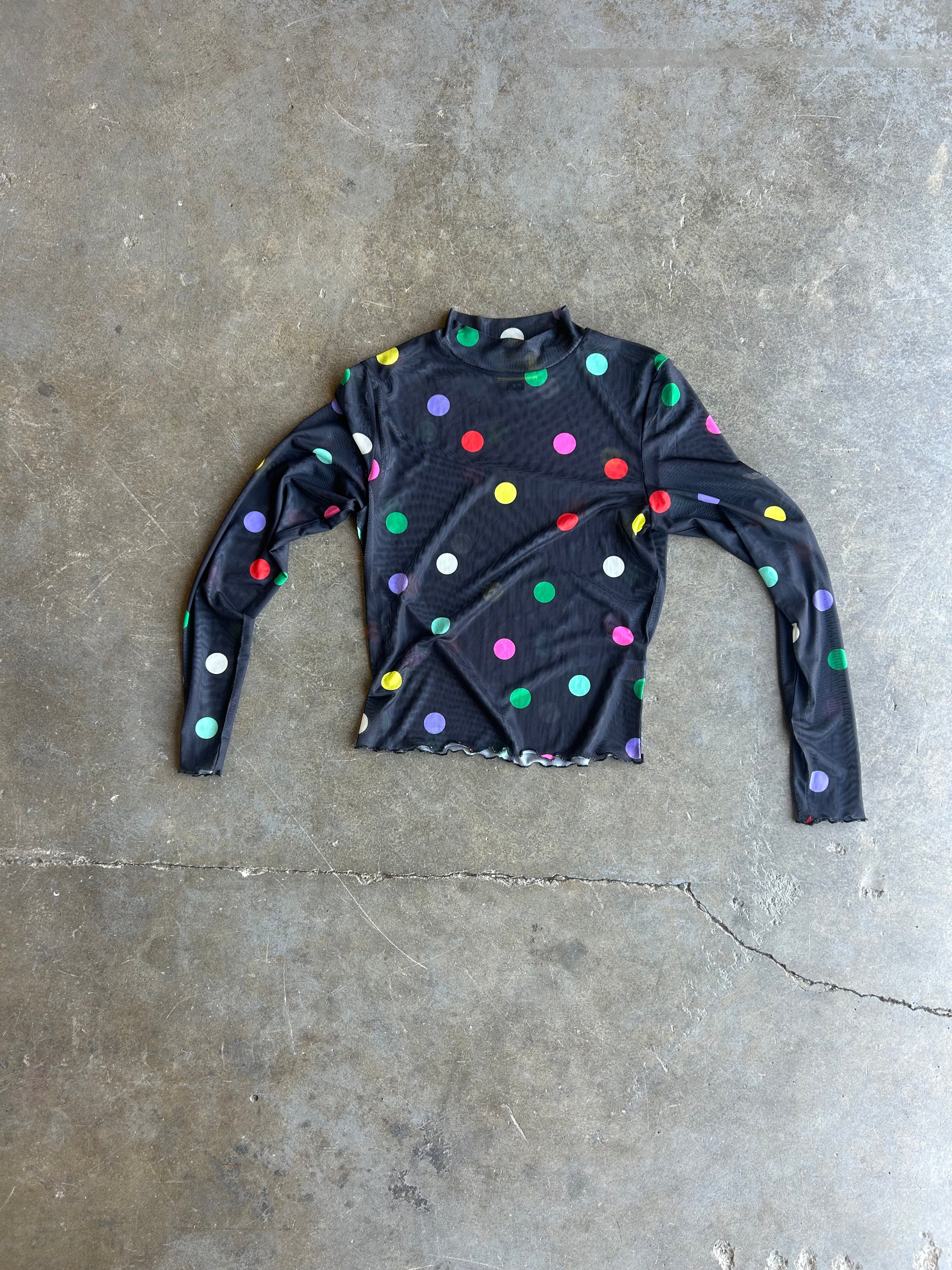 A black long-sleeve mock neck shirt with colorful polka dots, laid flat on a gray concrete floor
