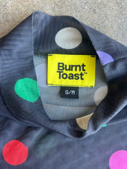 Close-up of a Burnt Toast garment collar showing a yellow brand label and a dark gray base with multicolored polka dots in green, red, pink, beige, and purple