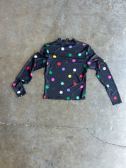 A black long-sleeve shirt with colorful polka dots in red, green, yellow, blue, pink, and white, laid flat on a gray concrete floor