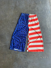 A pair of cropped athletic shorts laid flat on a gray concrete floor, featuring a split design: one half has a blue leopard print pattern and the other half has red and white horizontal stripes
