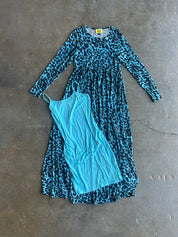 A long-sleeve blue and black leopard print dress laid flat on a concrete floor, with a light blue slip dress placed on top of it