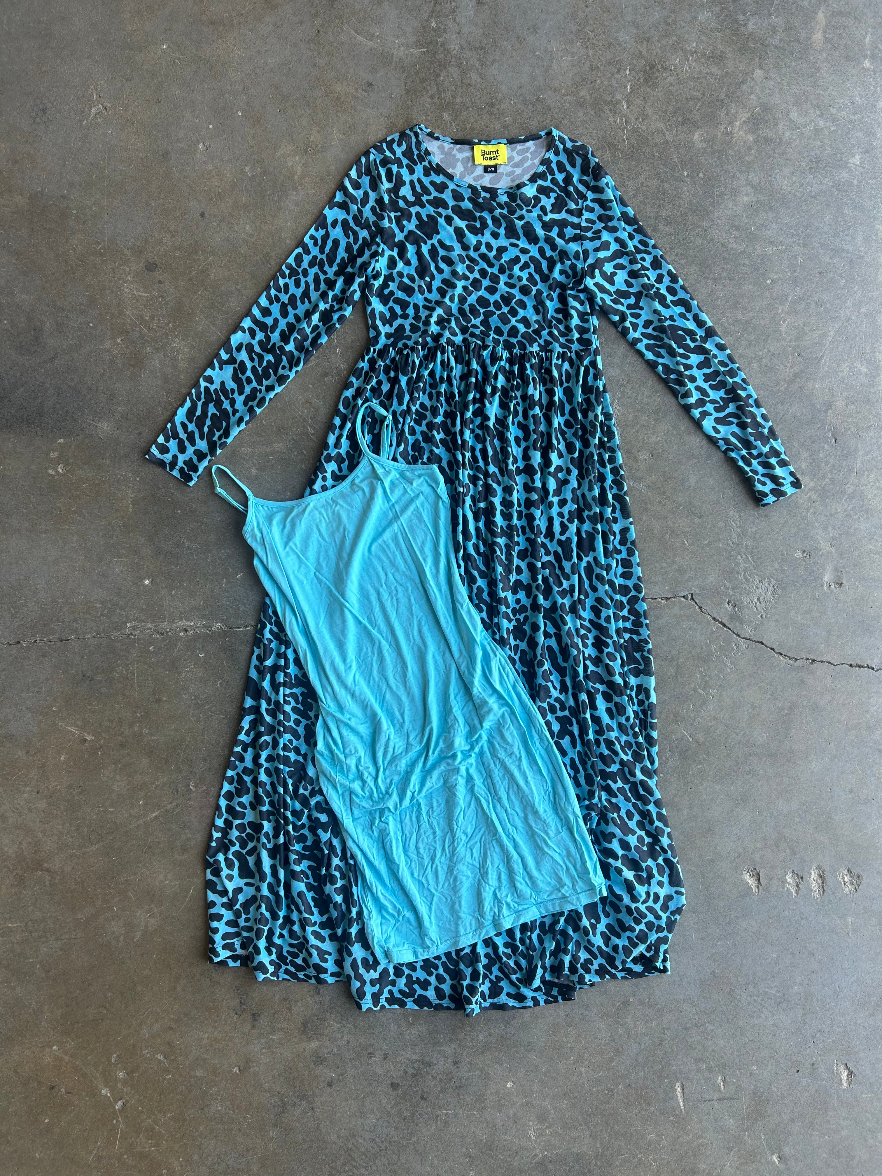 A long-sleeve blue and black leopard print dress laid flat on a concrete floor, with a light blue slip dress placed on top of it