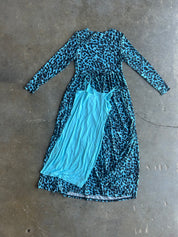 A long-sleeve midi dress with a blue and black leopard print, layered over a solid light blue tank top, laid flat on a gray concrete floor