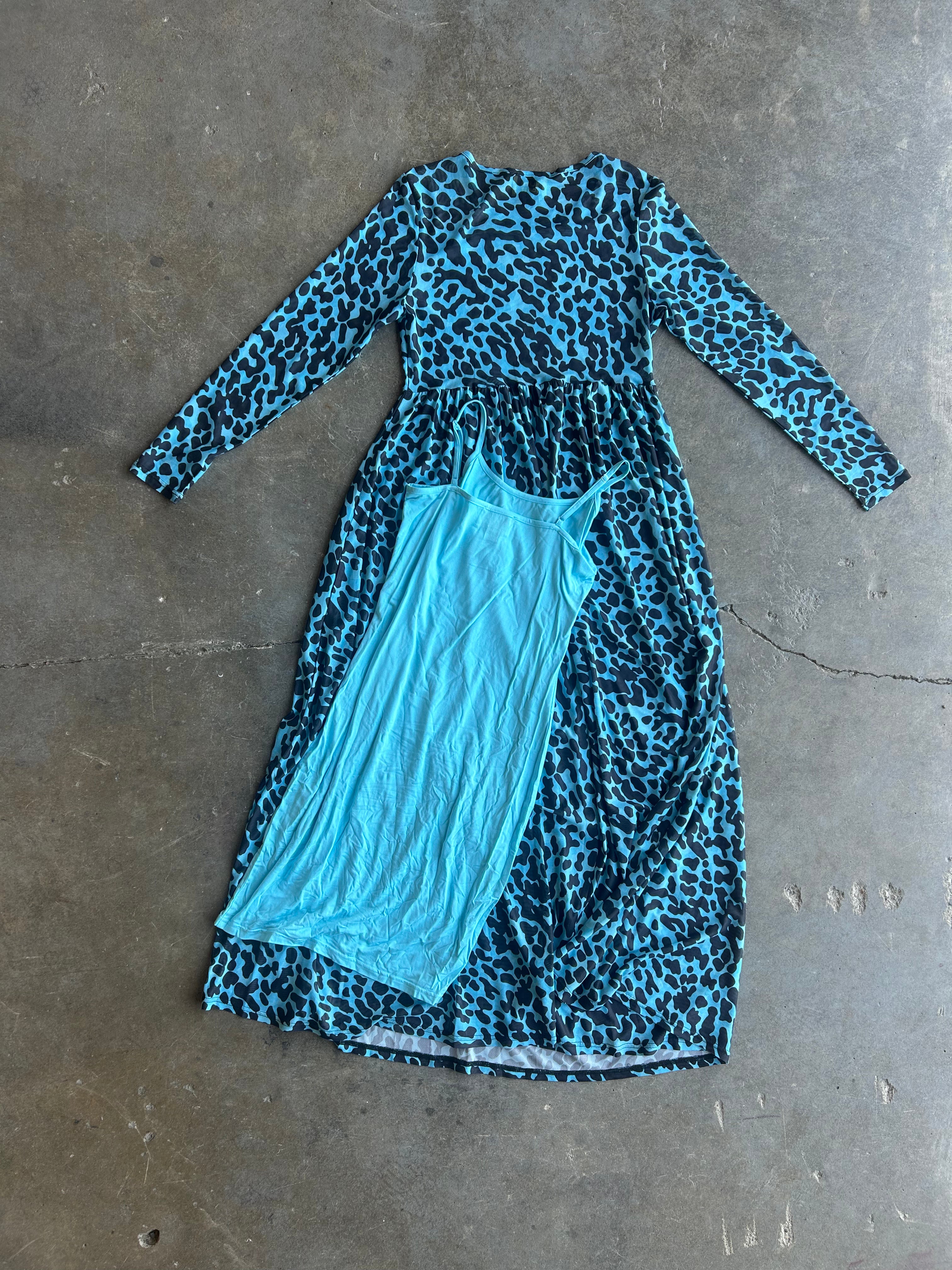 A long-sleeve midi dress with a blue and black leopard print, layered over a solid light blue tank top, laid flat on a gray concrete floor