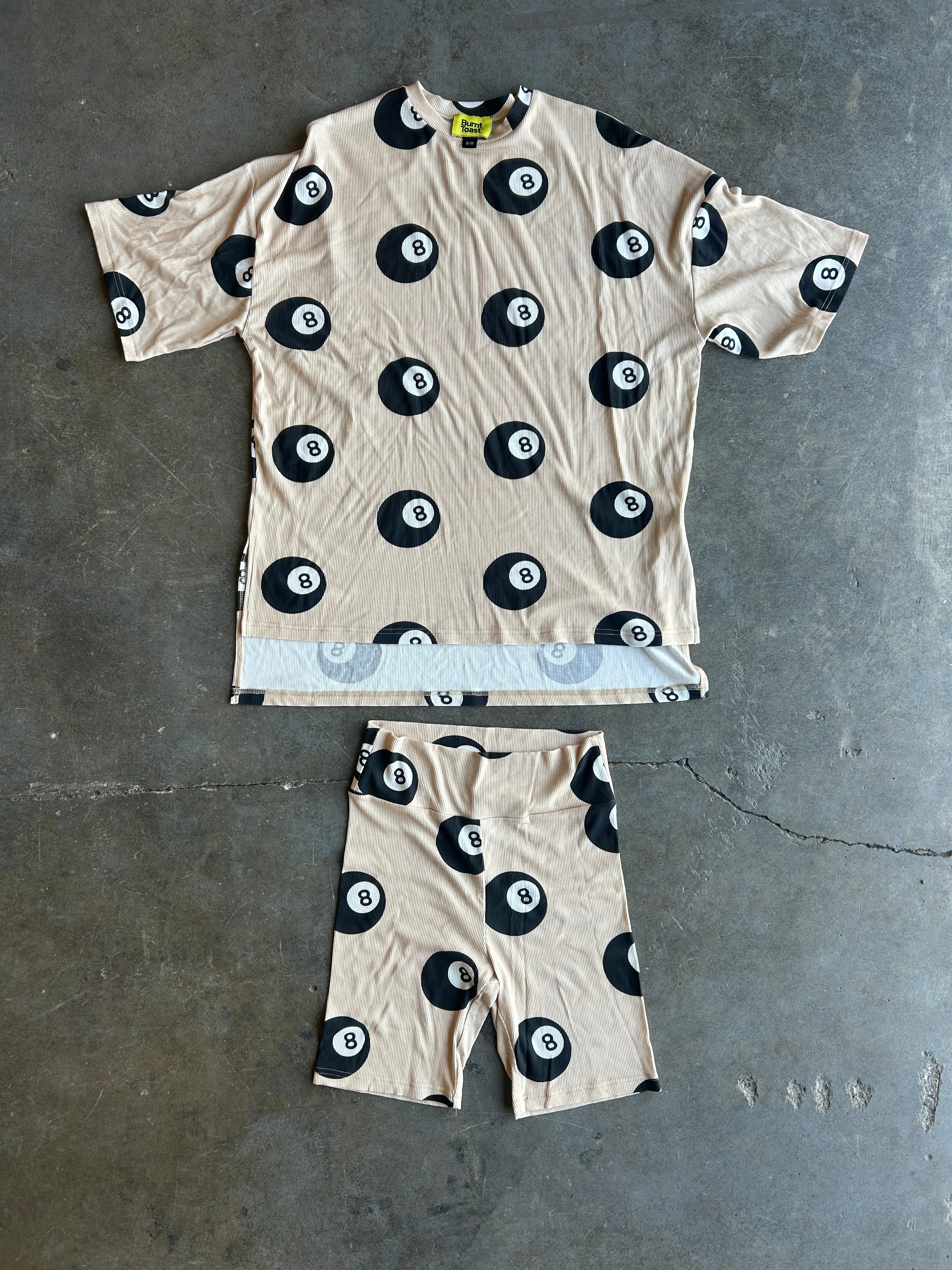 A matching short-sleeve t-shirt and shorts set laid flat on a gray concrete floor. The set features a beige base with a black and white 8-ball pattern, with a light blue and white striped hem detail on the shirt