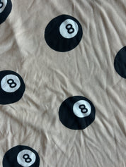Beige ribbed fabric with a repeating black 8-ball pool cue print, showing a wrinkled texture