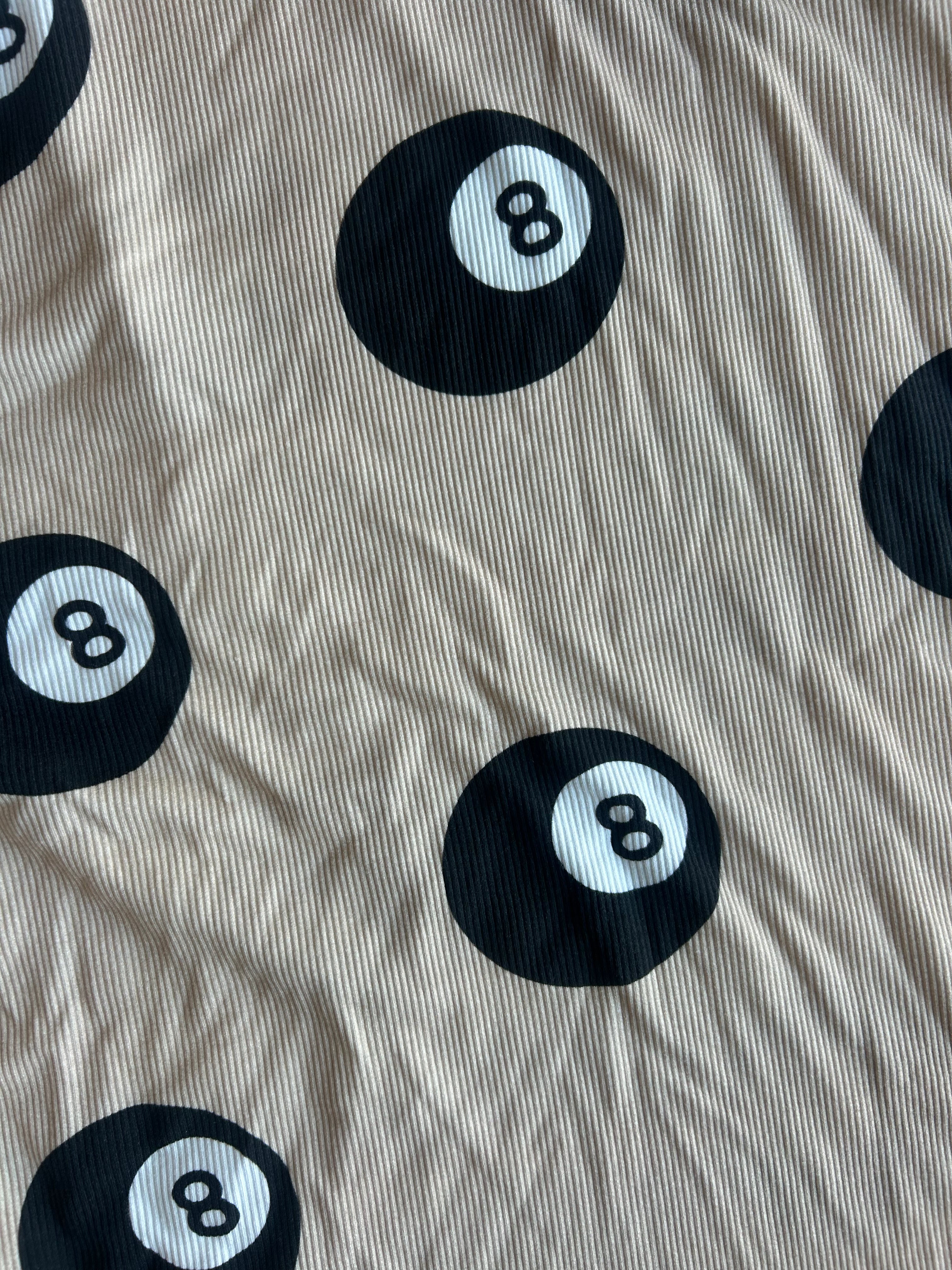 Beige ribbed fabric with a repeating black 8-ball pool cue print, showing a wrinkled texture