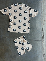 A matching beige short-sleeve t-shirt and shorts set with a black 8-ball pool pattern, laid flat on a gray concrete floor