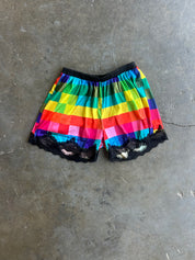 Rainbow checkered shorts with black lace trim, laid flat on a gray concrete floor.