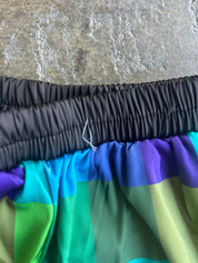 Close-up of a colorful striped fabric item, likely shorts or a skirt, showing a black elastic waistband and a multicolor body with green, blue, purple, and yellow stripes