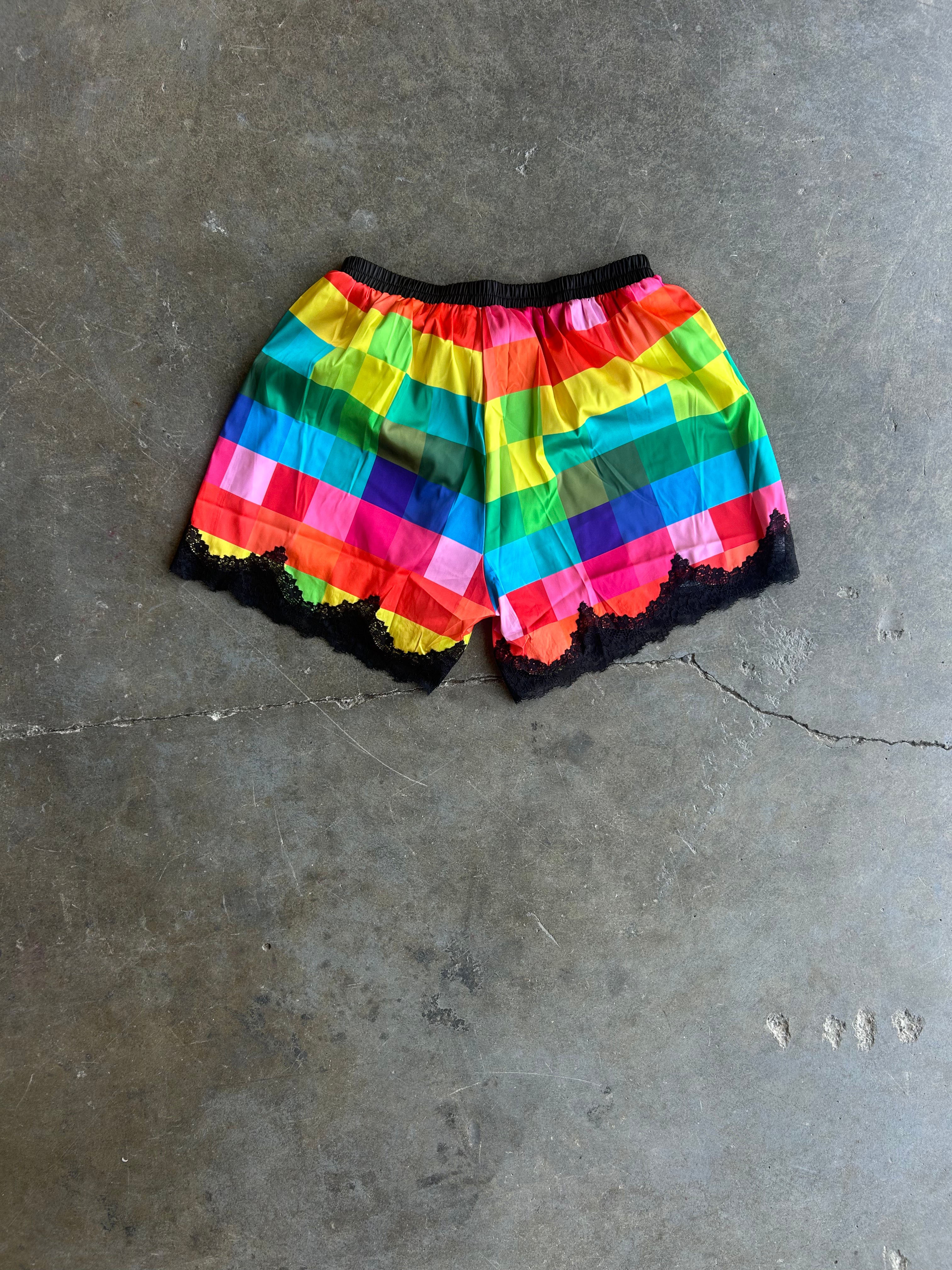 Rainbow striped ruffled shorts with black lace trim, laid flat on a gray concrete floor