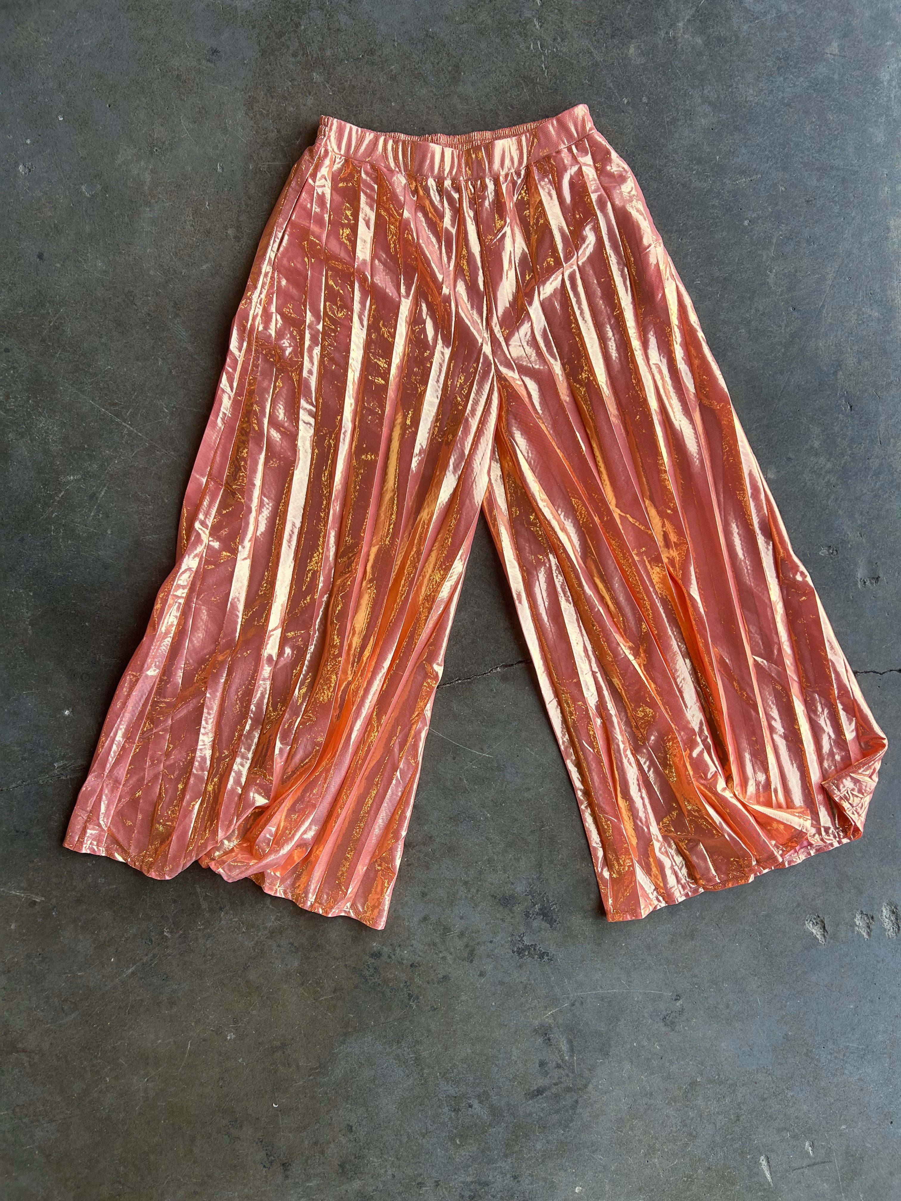 Metallic rose gold wide-leg cropped pants with a shiny, crinkled texture, laid flat on a dark gray concrete surface