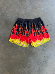 Black and red flame-print shorts with yellow lace trim, laid flat on a gray concrete floor
