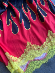 A close-up of a red garment featuring a navy blue flame print outlined in yellow, finished with a yellow lace hem