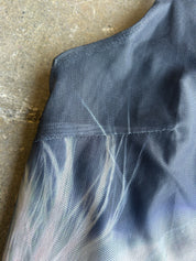 Close-up detail of a dark gray mesh garment with a subtle white and light blue abstract pattern, laid flat on a textured concrete surface