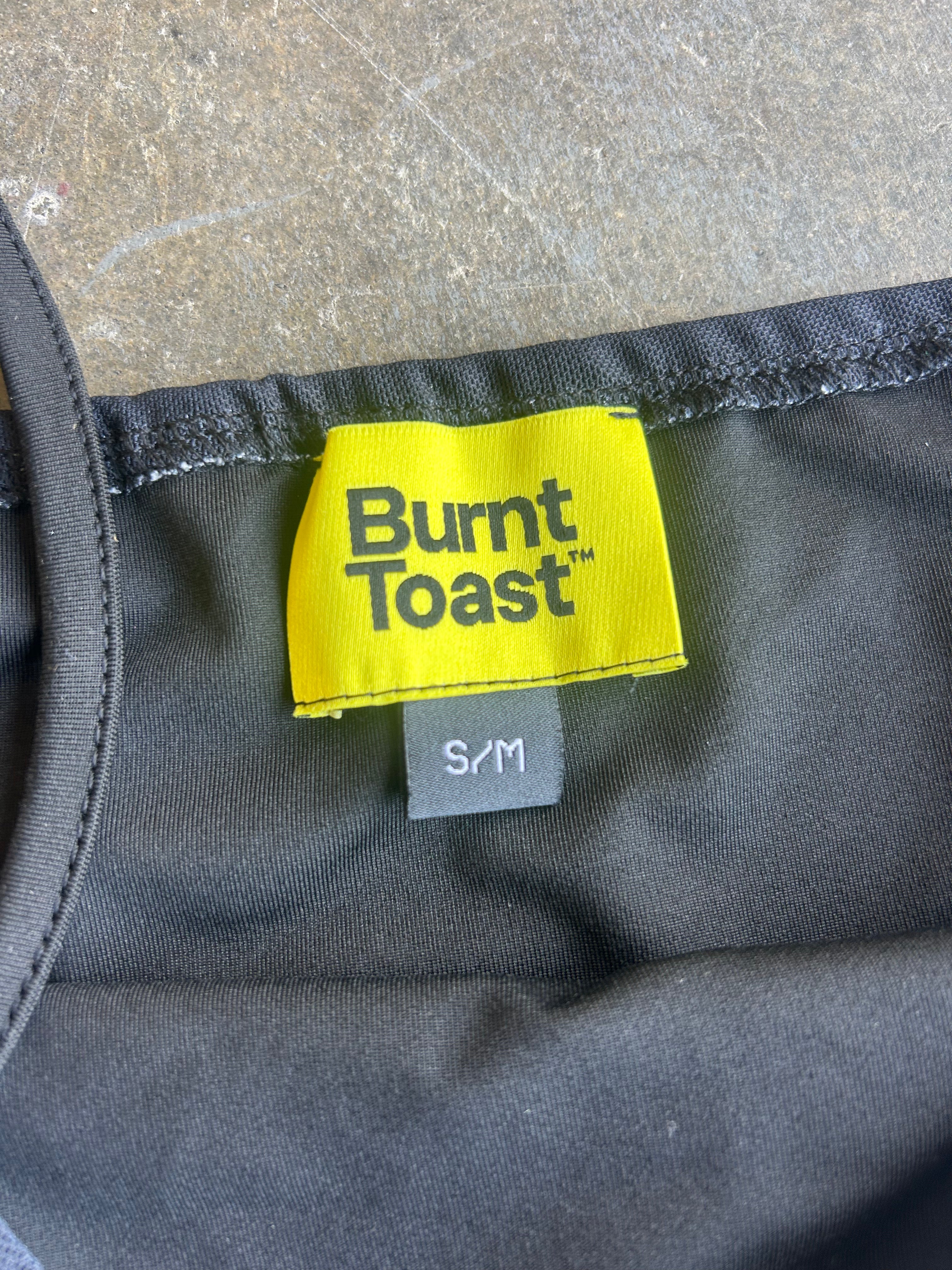 Close up of yellow Burnt Toast tag size S/M on a concrete surface