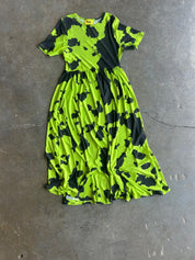 A short-sleeve midi dress with a bright neon lime green and black abstract camouflage pattern, laid flat on a gray concrete floor