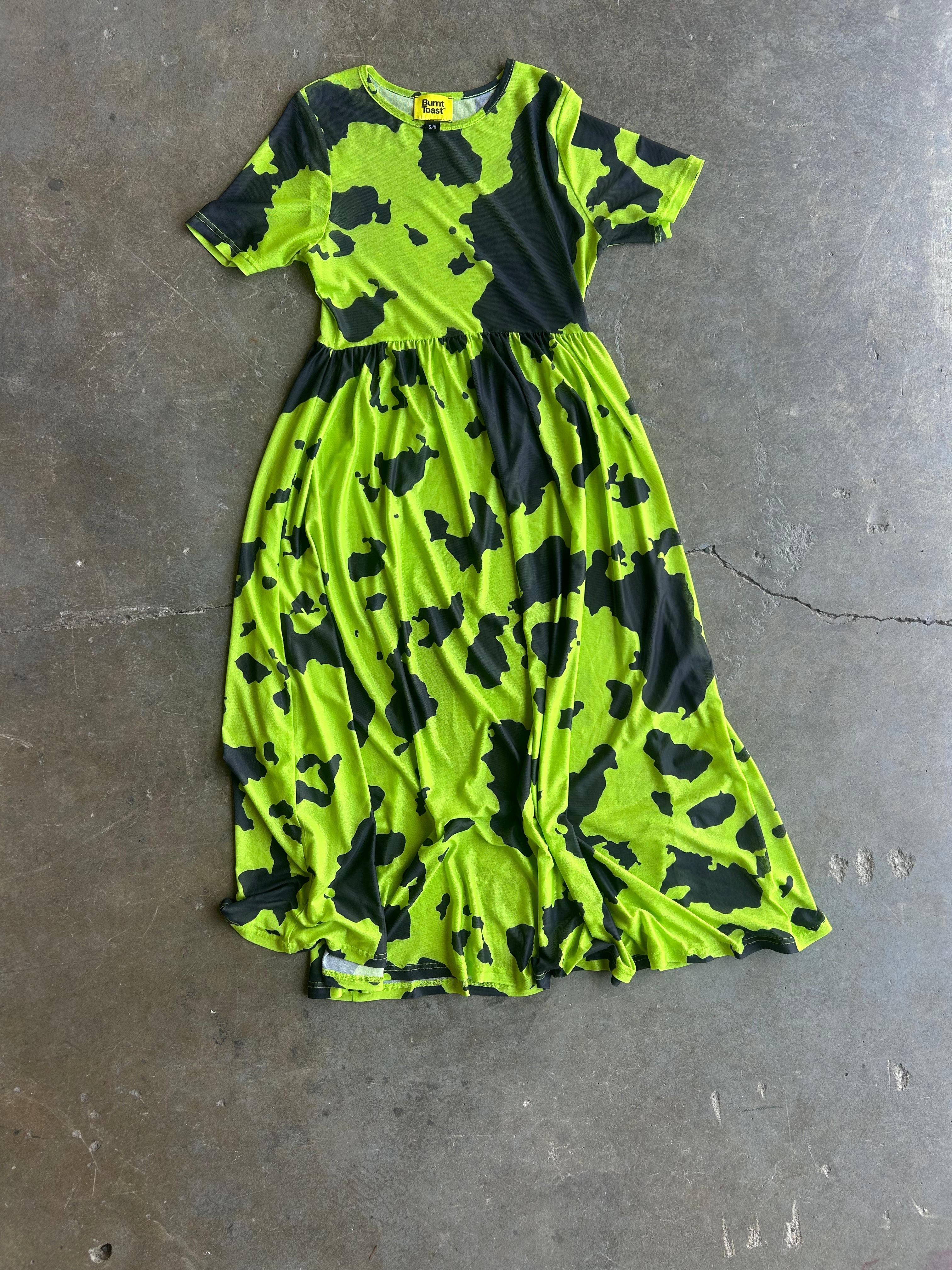 A short-sleeve midi dress with a bright neon lime green and black abstract camouflage pattern, laid flat on a gray concrete floor