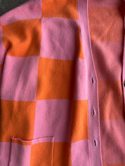 Close up of a pink and orange checkered cardigan, flat lay frontal view