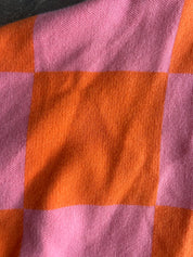 A close-up of a woven textile with a pink and orange checkered pattern, showing the fabric texture and folds