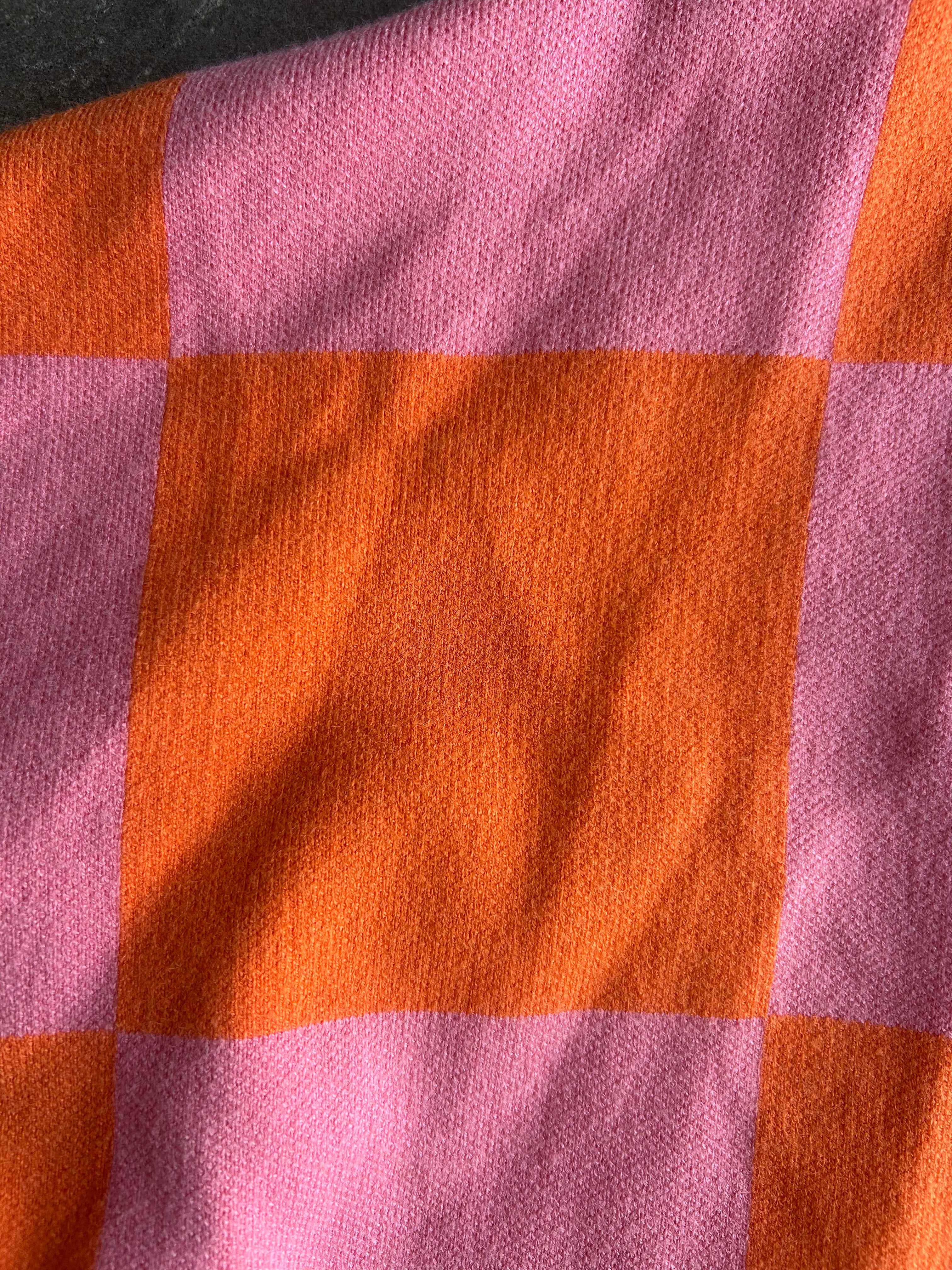 A close-up of a woven textile with a pink and orange checkered pattern, showing the fabric texture and folds