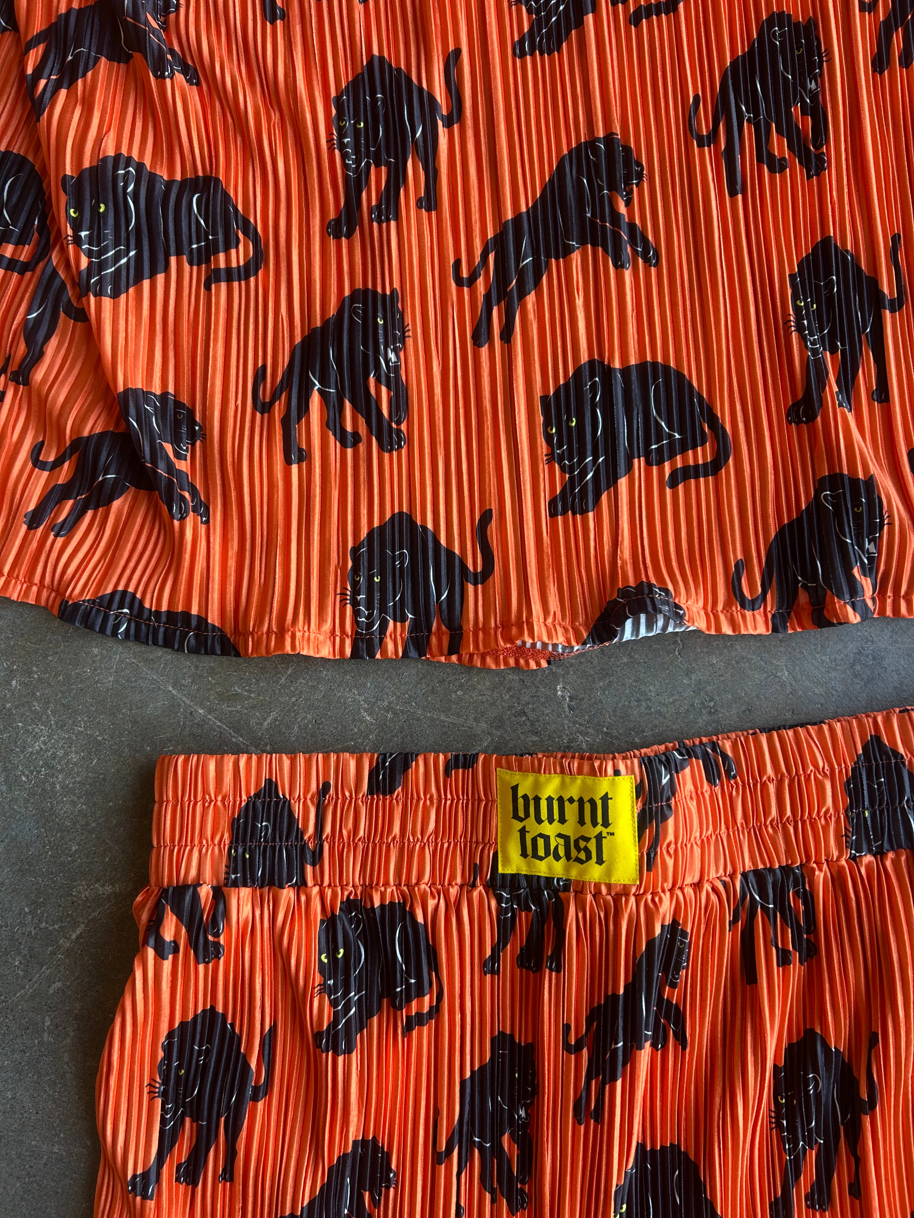 Close-up of a two-piece matching set featuring a vibrant orange pleated fabric with a black animal print and a yellow 'burnt toast' brand label