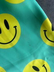 A close-up of a teal fabric with a repeating yellow smiley face pattern, showing the texture of the material and the print details